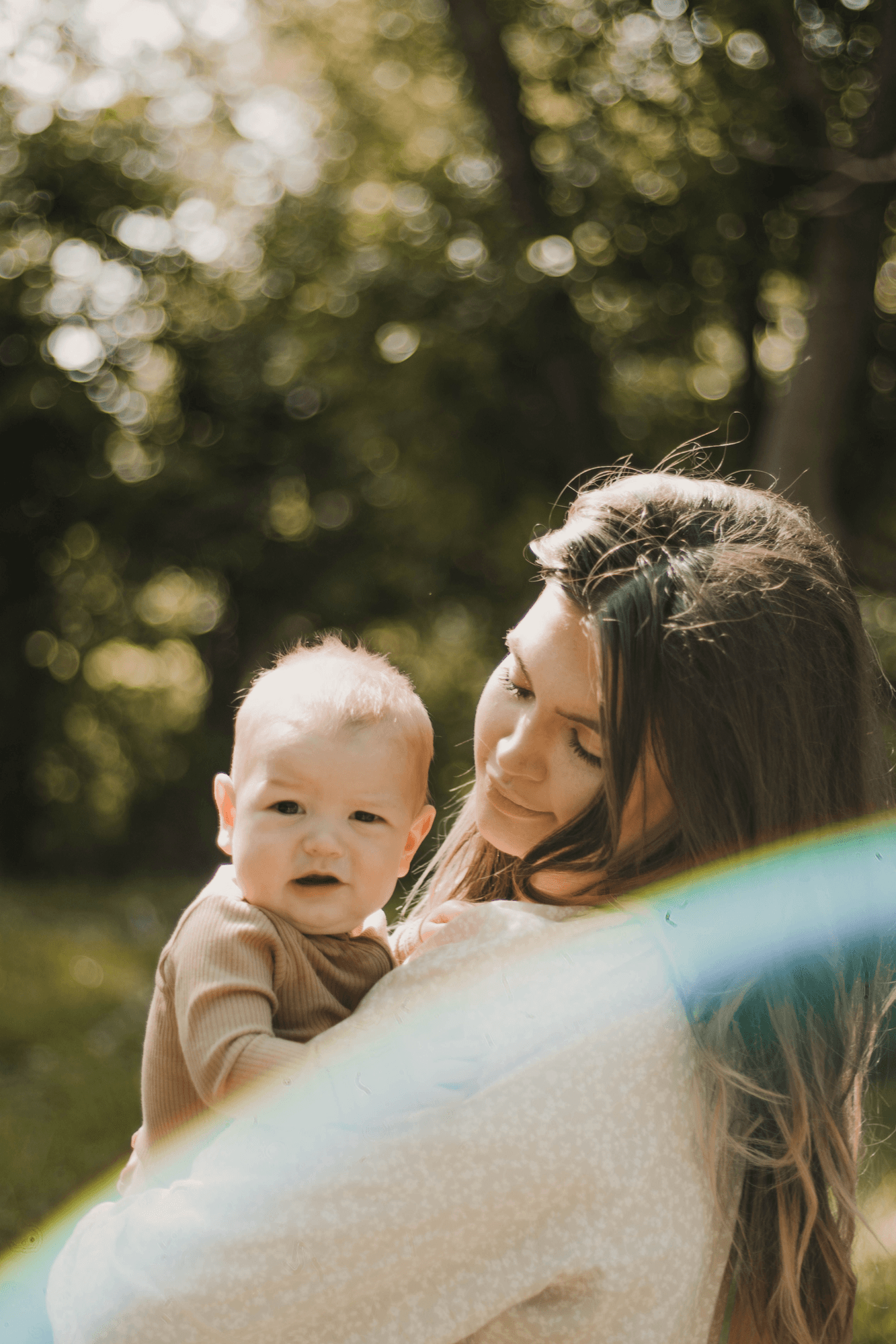 Madre sonriendo con su bebé en brazos en un bosque